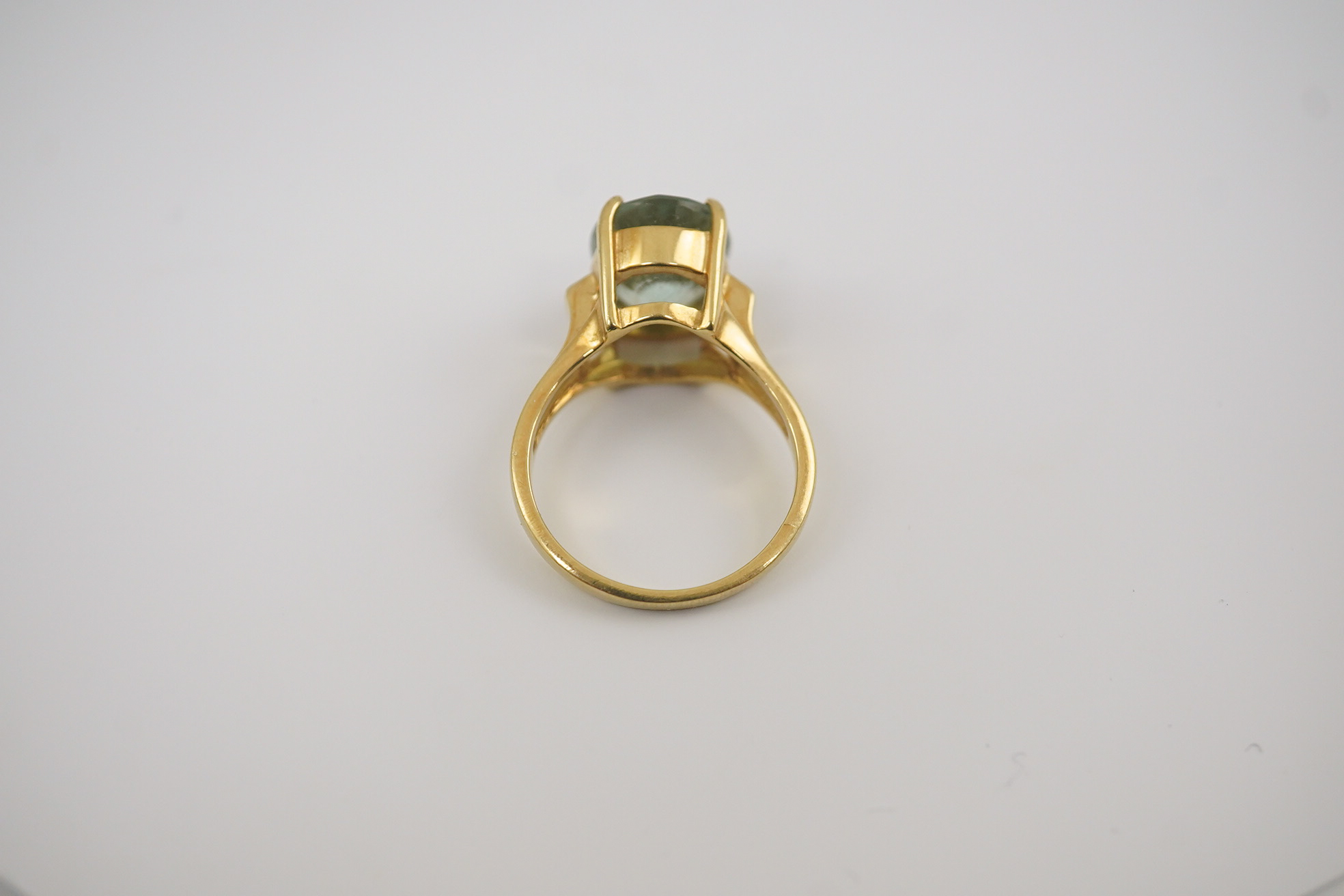 A modern 18ct gold and oval cut pale green tourmaline set dress ring, with two stone diamond chip set shoulders